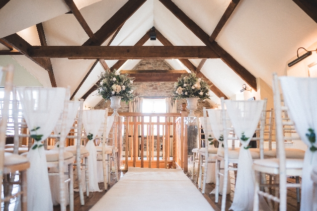 A rustic room set up for a wedding ceremony with white chairs and flowers