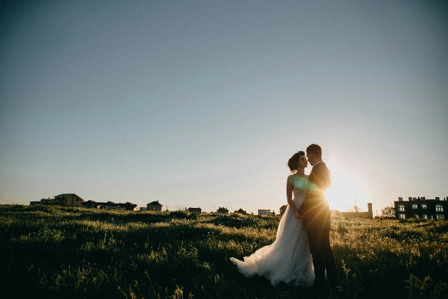 A man and woman embracing in a field as the sun sets