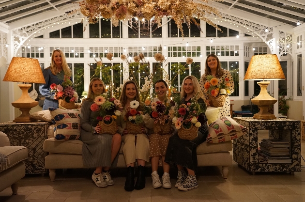 Six women in a living room holding colourful bouquets