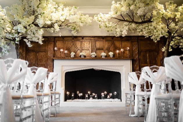 A large white fireplace with clear chairs in front of it and a blossom arch