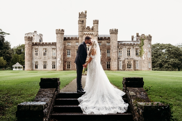 A bride and groom kissing in front of a castle