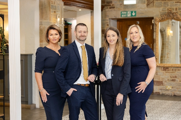 A man and three women dressed smartly smiling at the camera