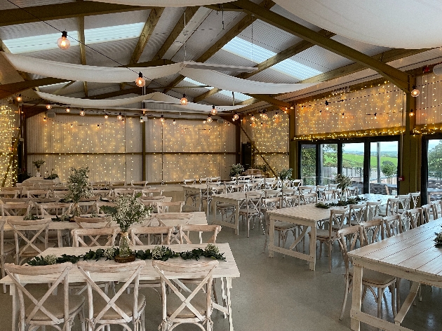 A barn-like building decorated with wooden tables, chairs and fairy lights