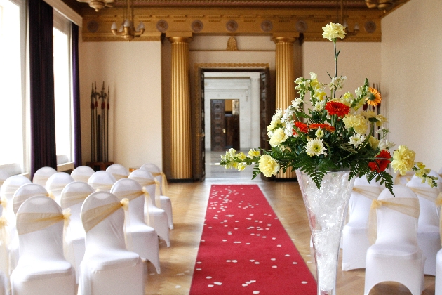 A light room with gold columns and white chairs lining an aisle