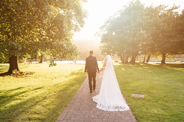 A bride and groom walking hand-in-hand on some grass