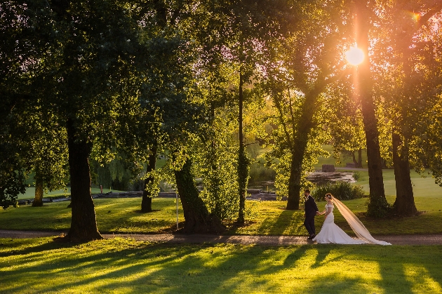 A bride and groom walking through a forest as the sun sets