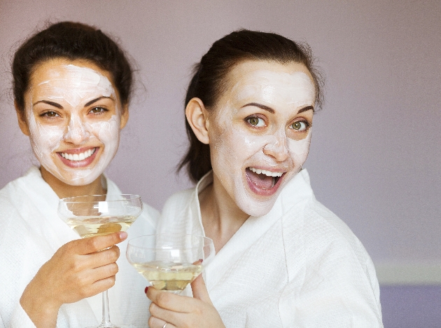 Two women smiling at the camera while wearing robes and holding a glass of drink each