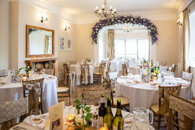 A light-filled room decorated with white, round tables and flowers