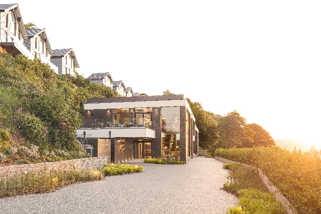 The exterior of a sleek black and white building with lots of windows surrounded by foliage