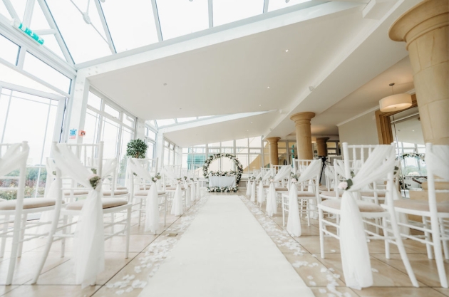 A light-filled room with white chairs lining an aisle