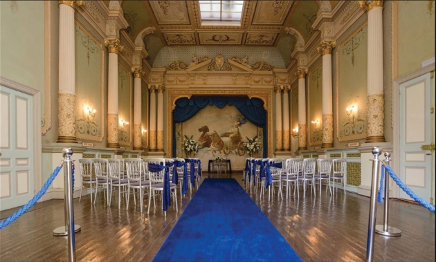 A gold room with silver chairs lining a blue aisle runner