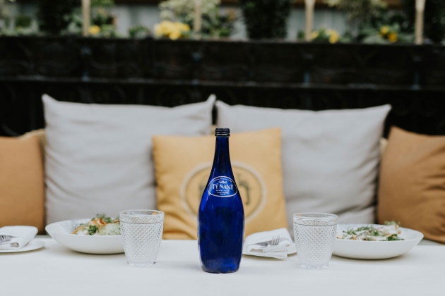 A blue bottle placed on a table with a sofa behind it